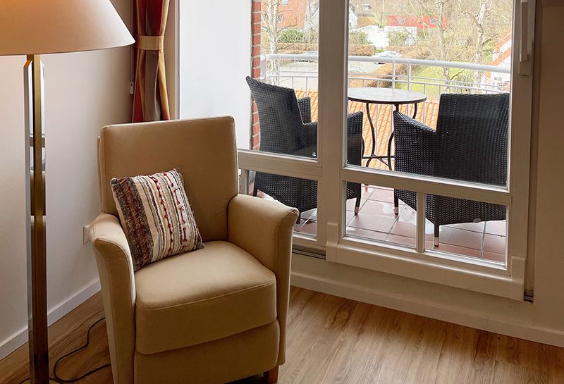 Doppelzimmer Süd-West Loggia Doppelzimmer mit Loggia, auf der Loggia zwei Sessel und ein kleiner runder Tisch, Blick zur Süd-Westseite, vor der Loggiatür steht ein Lesesessel mit Kissen, daneben eine Stehlampe