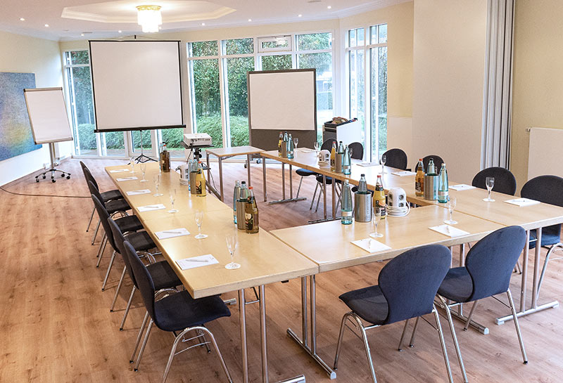 Tagungsräume Kletkamp und Neudorf Tagungsraum Lütjenburg (Kletkamp und Neudorf) im Hotel Hohe Wacht, Bestuhlung in U-Form, eingedeckt mit Gläsern, Getränken, Schreibblöcken, im Hintergrund Beamer, Leinwand, Flipchart, Pinwand mit Papier