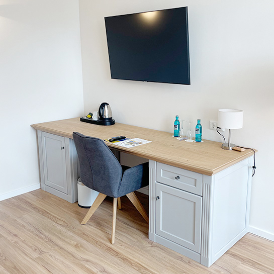Doppelzimmer Schreibtisch Doppelzimmer Schreibtisch mit Stuhl an der Wand, über dem Schreibtisch ein TV-Gerät, auf dem Schreibtisch Lampe, Welcome Tray Kaffee/Tee, Wasserkocher, Minibar, Fernbedienung TV, Prospekt