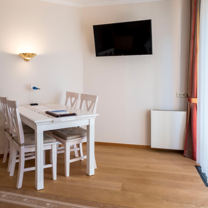 2-Zimmer-Komfortappartement Essbereich 2-Zimmer-Komfortappartement Essbereich, Laminatboden, Esstisch mit vier Stühlen, an der Wand Lampe und TV-Gerät