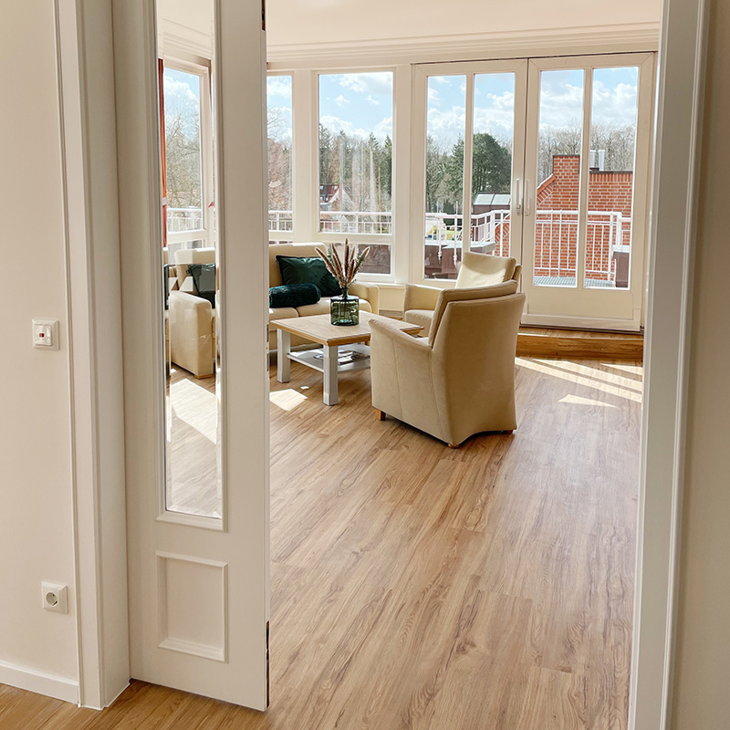 Kurparksuite Eingangsbereich Kurpark-Suite Eingangsbereich, Durchgang zum Schlaf- und Wohnbereich, Blick auf die Sitzecke mit Sofa, Sessel und Tisch, hinter der Sitzecke Fensterfront mit Terrassentür zum Balkon