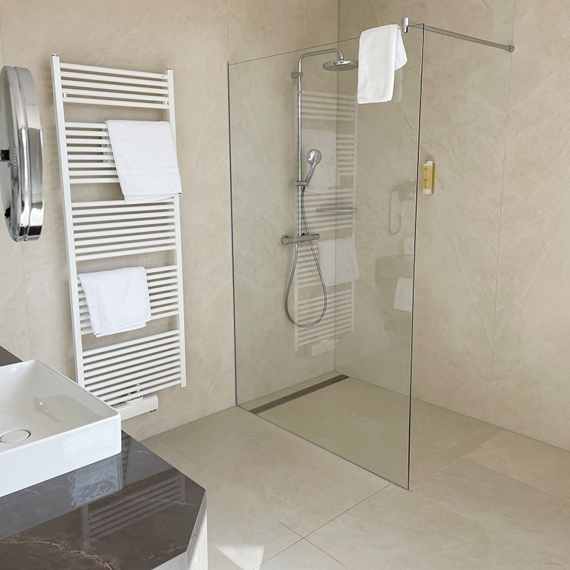 Kurpark-Suite Bad Bad Kurpark-Suite, links Waschtisch mit Waschbecken und Kosmetikspiegel, an der Wand daneben Handtuchheizkörper, Dusche mit Glaswand, durch die Glaswand sieht man die Duscharmatur