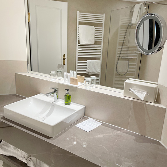 Turmzimmer Bad Bad im Turmzimmer mit Waschbecken, Seifenspender, Kosmetikspiegel, Kosmetikproben, Handtüchern, im Spiegel spiegelt sich Dusche und Handtuchheizkörper sowie die Tür