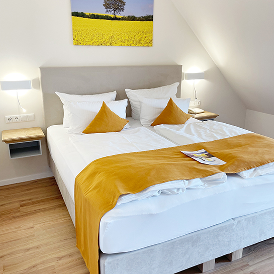 Turmzimmer Boxspringbett Schlafbereich im Turmzimmer, Boxspringbett mit Kopfende an der Wand, darüber Leinwand mit Rapsmotiv, links und rechts vom Bett Lampen und Ablageflächen