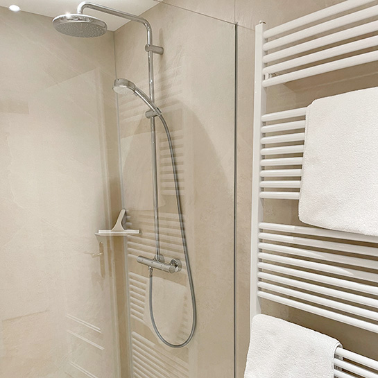 Turmzimmer Dusche Dusche mit Glaswänden, durch die Glaswand sieht man die Armatur mit großer und kleiner Duschbrause, rechts neben der Dusche hängt der Handtuchwandtrockner mit weißen Handtüchern