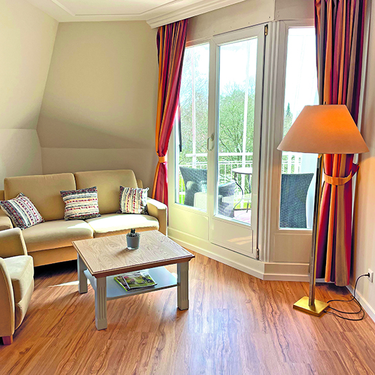 Turmzimmer Loggia links Sitzecke mit Sofa, Tisch und Sessel, daneben Ausgang zur Loggia, auf der Loggia Sitzmöglichkeiten sowie ein kleiner Tisch, rechts neben dem Ausgang zur Loggia steht eine Stehlampe