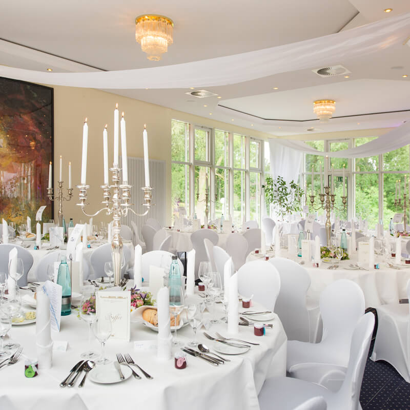 prunkvoll geschmückter Ballsaal mit Tisch auf denen Blumengesteck, Silberbesteck und Kerzenleuchter sind