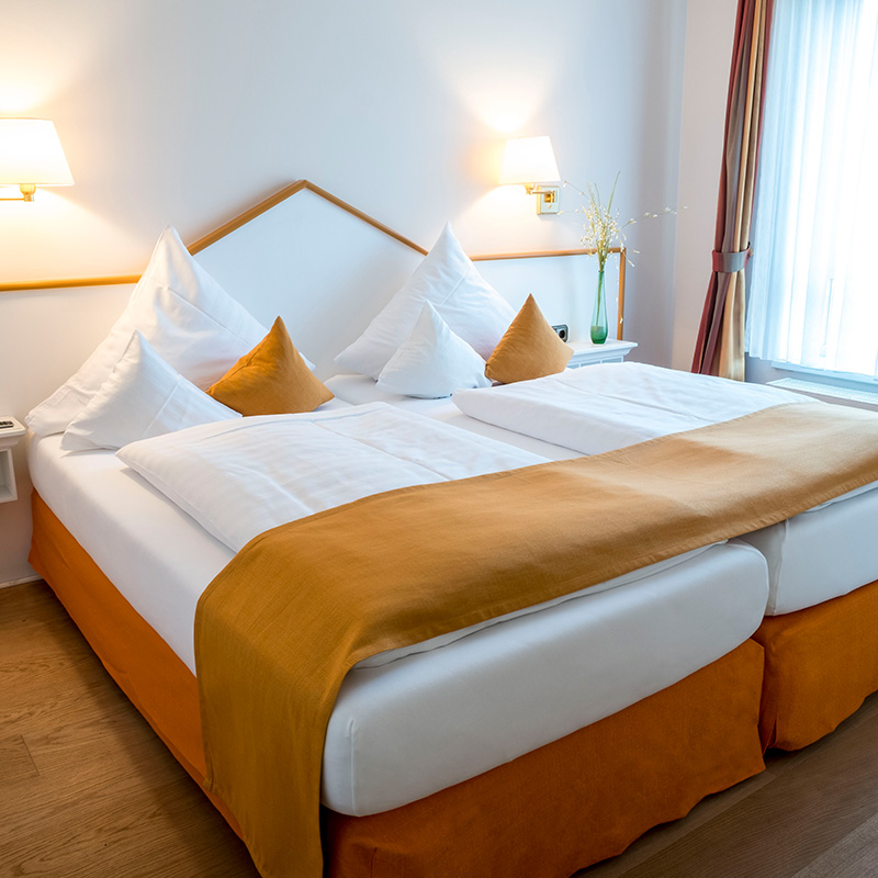 großes gemütliches Bett mit gelben Dekokissen und großer Leinwand über dem Bett