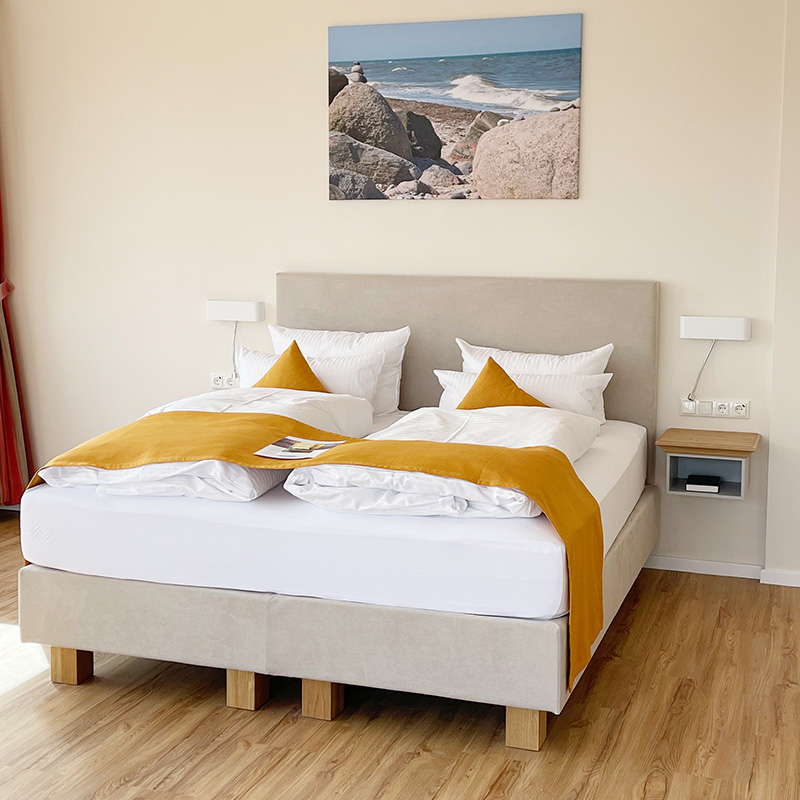 Ostsee Suite Bett mit fluffiger weißer Bettwäsche, gelben Dekokissen und gelben Läufer